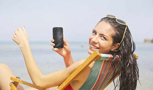Woman sat on a beach holding her mobile phone